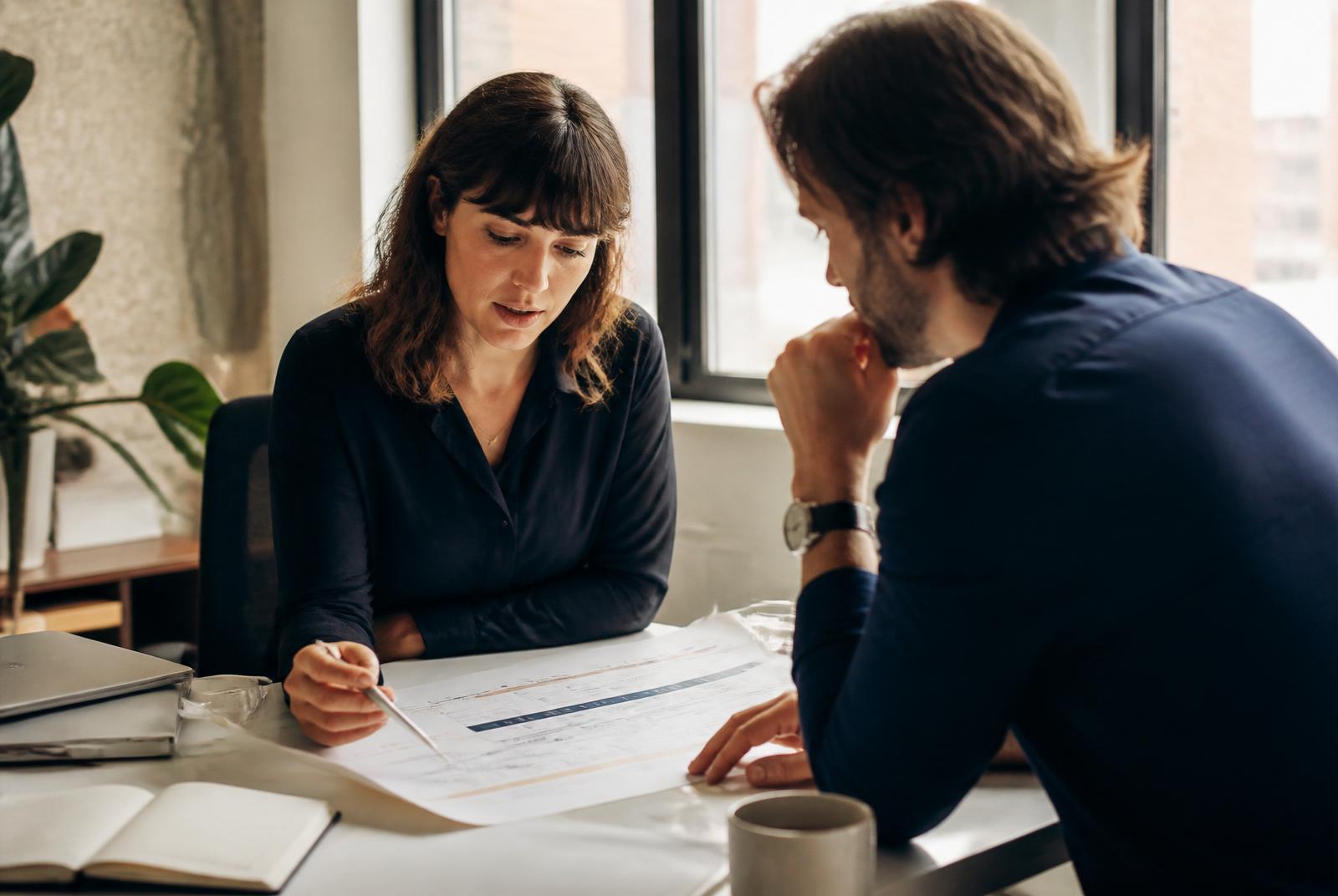 Two colleagues reviewing a printed project timeline together at a bright workspace