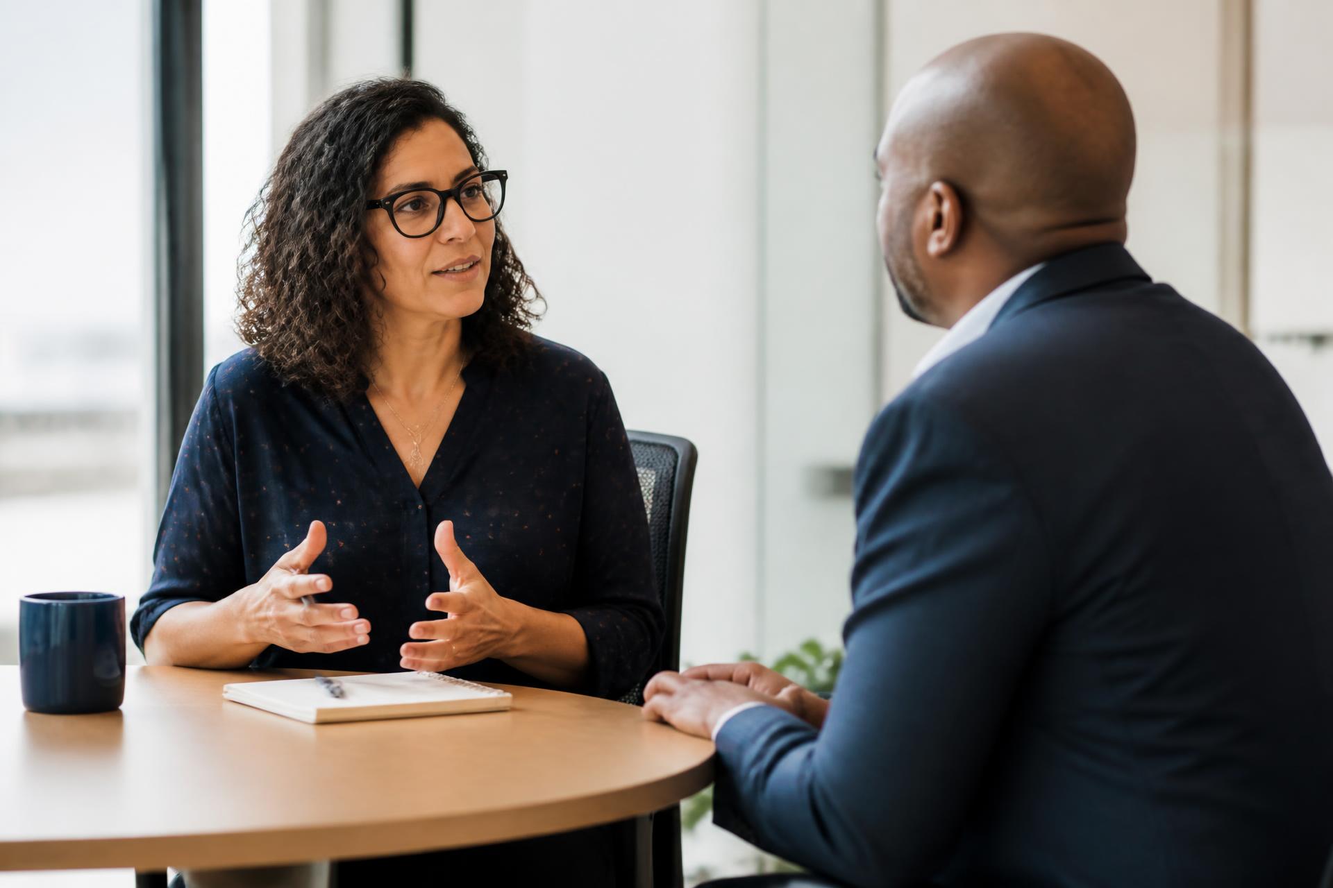 Two professionals in a focused one-on-one conversation across a small table by a window