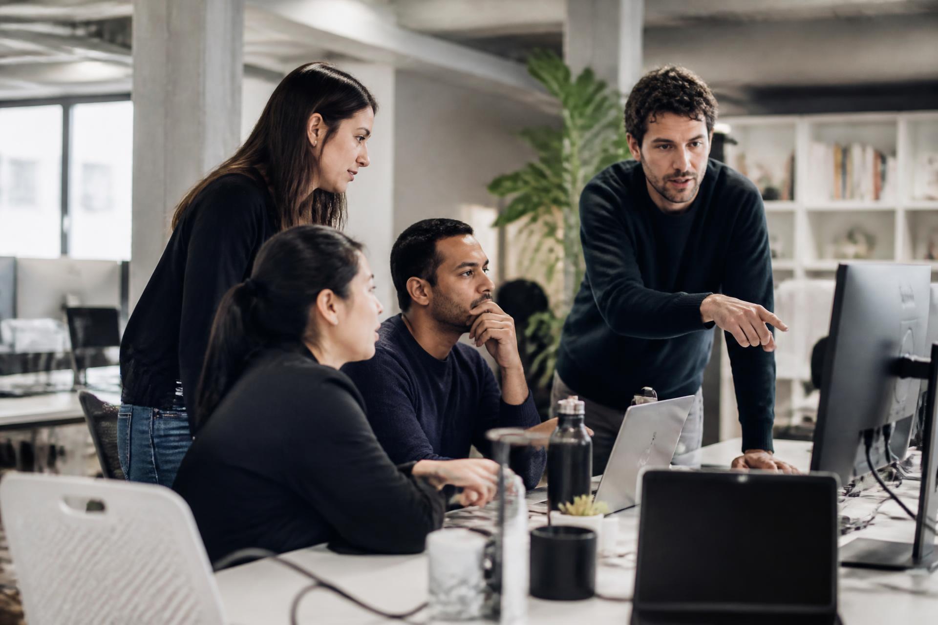 A modern technology team collaborating around monitors in a real workspace